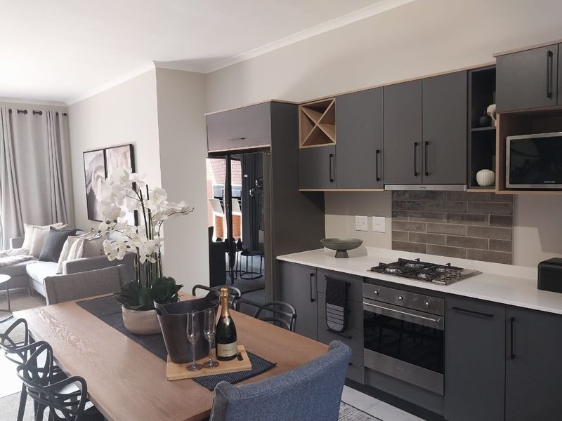 Modern open-plan living area featuring a contemporary kitchen with dark cabinetry, gas hob, built-in oven, and sleek quartz countertops.