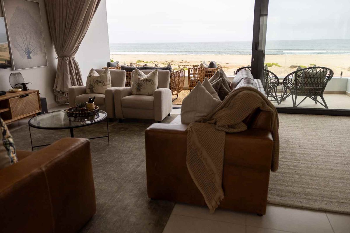 Spacious living room featuring large sliding glass doors that open onto a balcony with direct ocean views and a glass balustrade.