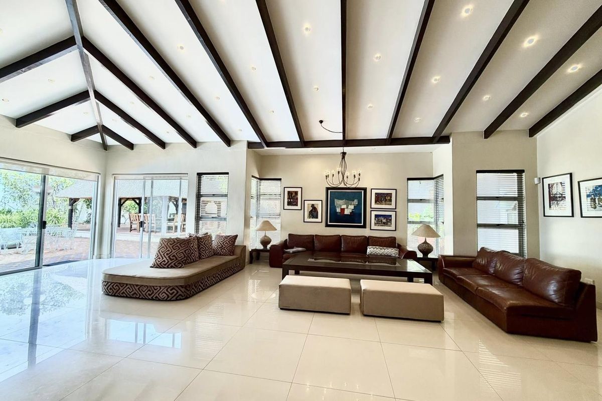 Spacious living room featuring high vaulted ceilings with exposed timber beams, polished porcelain floor tiles, and large sliding glass doors leading to the patio.