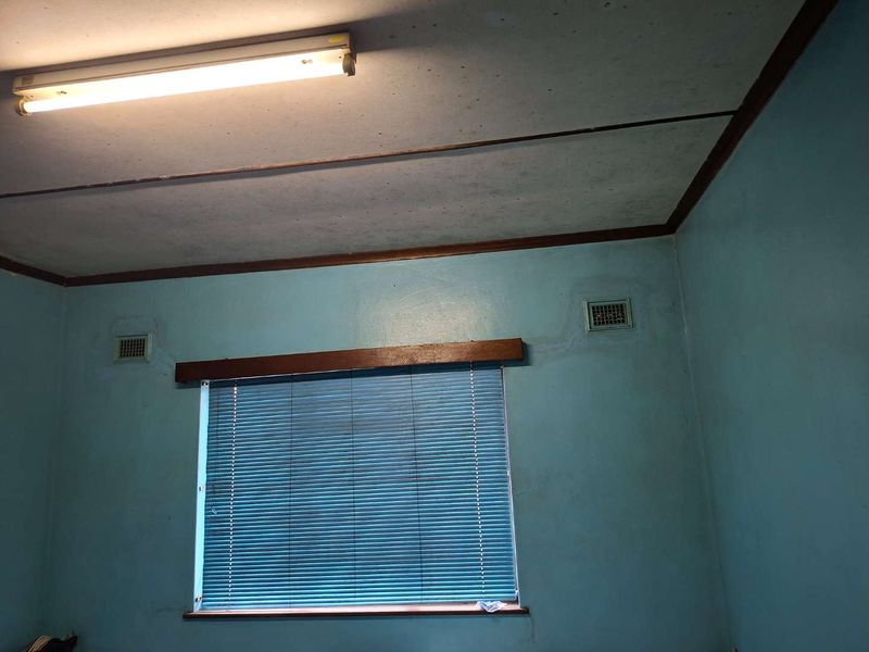 A vacant bedroom featuring blue walls, timber trim, and ceiling-mounted lighting, showing signs of wear and water staining on the wall surfaces.