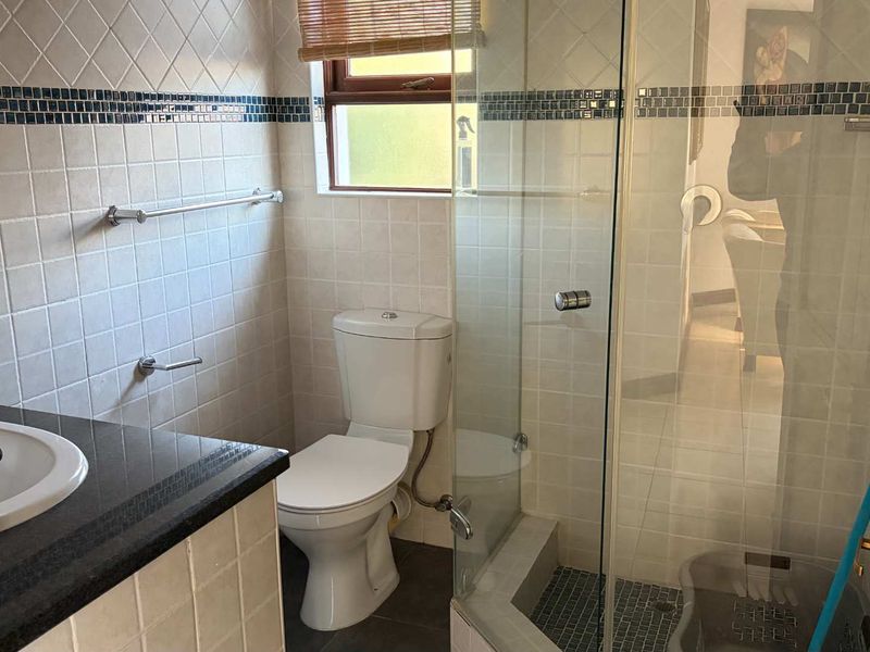 A functional bathroom featuring a vanity with a granite countertop, a toilet, and a glass-enclosed shower with tiled finishes.