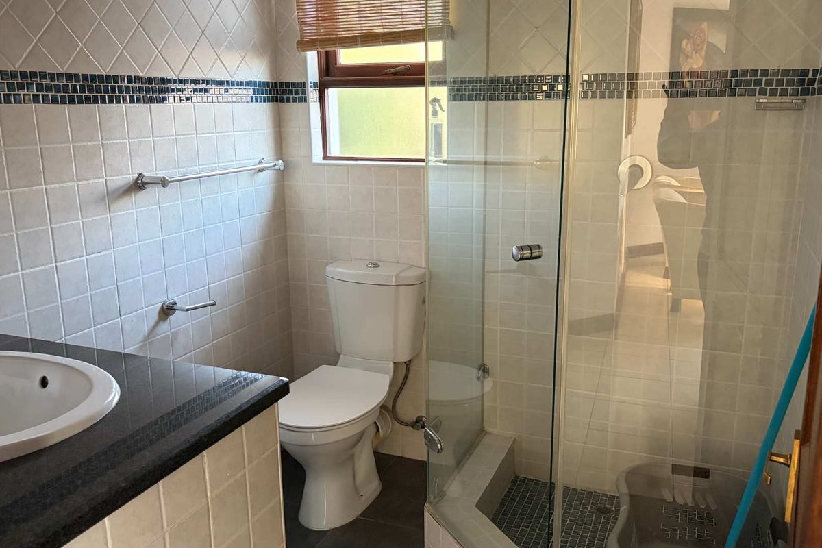 A functional bathroom featuring a vanity with a granite countertop, a toilet, and a glass-enclosed shower with tiled finishes.