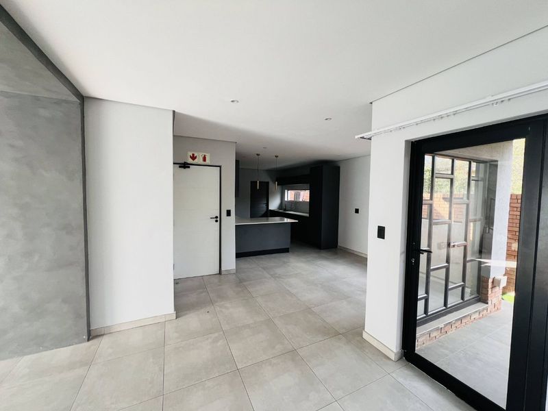 Modern open-plan living area featuring neutral tiled flooring, recessed lighting, and a sleek kitchen with built-in cabinetry and island, leading to an outdoor space.