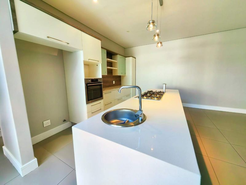 Modern kitchen featuring a central island with a gas hob and sink, complemented by built-in cabinetry, an integrated oven, and contemporary pendant lighting.