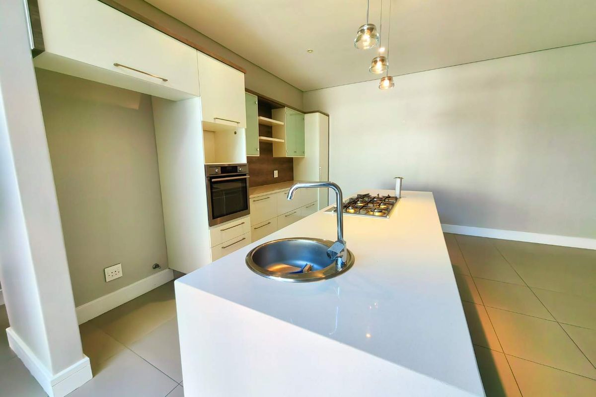 Modern kitchen featuring a central island with a gas hob and sink, complemented by built-in cabinetry, an integrated oven, and contemporary pendant lighting.