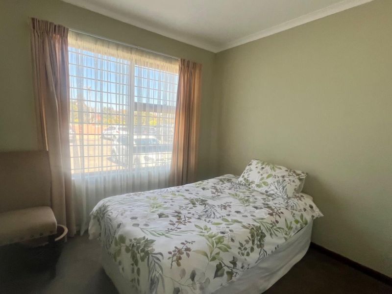 A standard bedroom featuring neutral wall paint, carpeted flooring, and a large window with installed curtain rails.