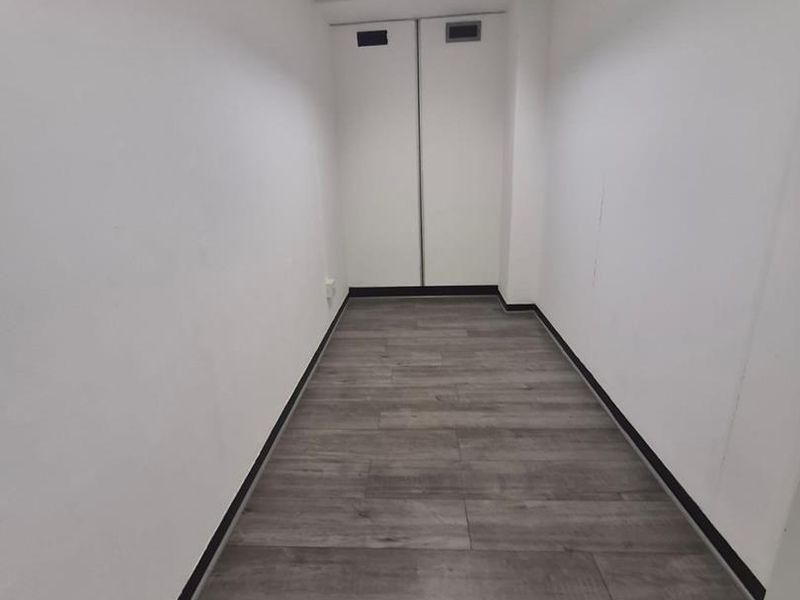 A clean, empty office hallway featuring modern grey laminate flooring, a drop ceiling with integrated lighting, and built-in storage cupboards.