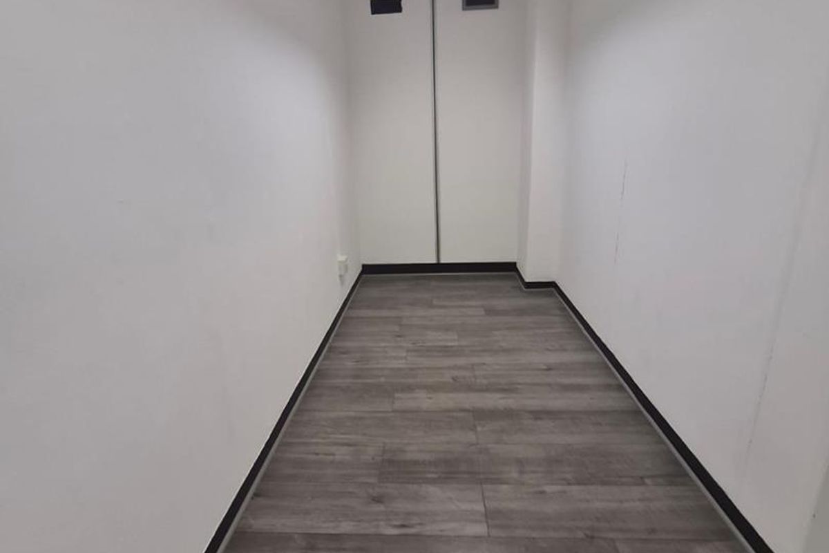A clean, empty office hallway featuring modern grey laminate flooring, a drop ceiling with integrated lighting, and built-in storage cupboards.