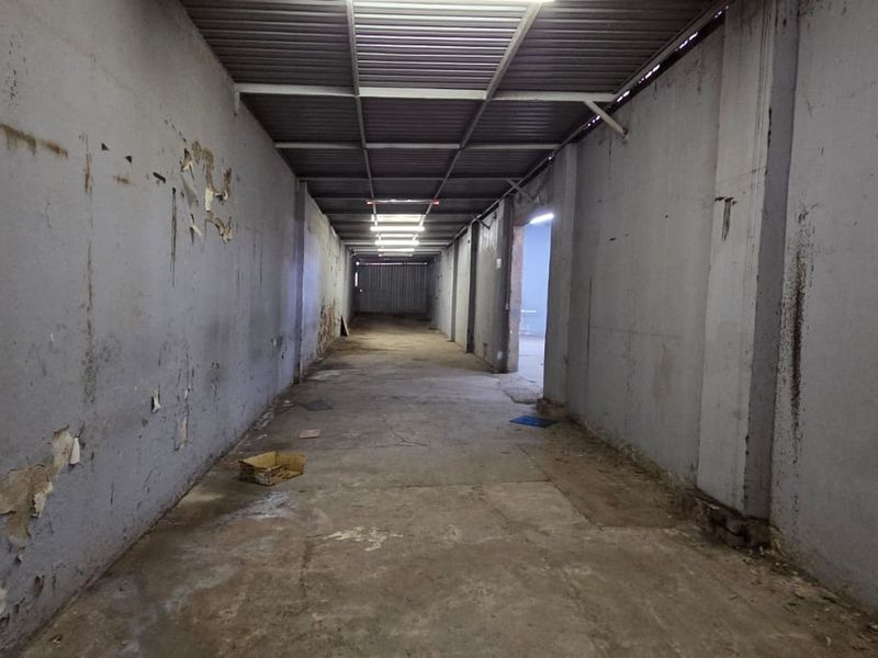 A long, industrial-style hallway featuring exposed metal roofing, concrete flooring, and fluorescent lighting, currently in need of cosmetic refurbishment.
