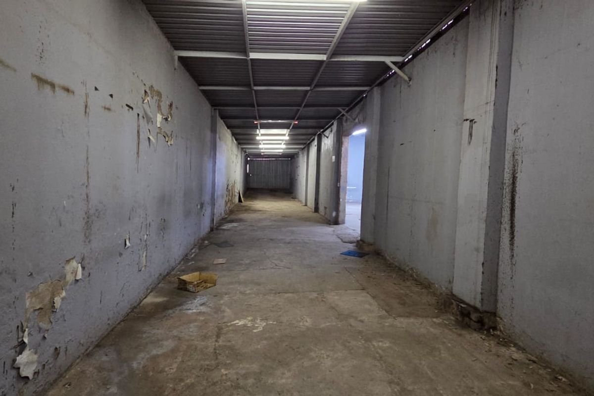 A long, industrial-style hallway featuring exposed metal roofing, concrete flooring, and fluorescent lighting, currently in need of cosmetic refurbishment.