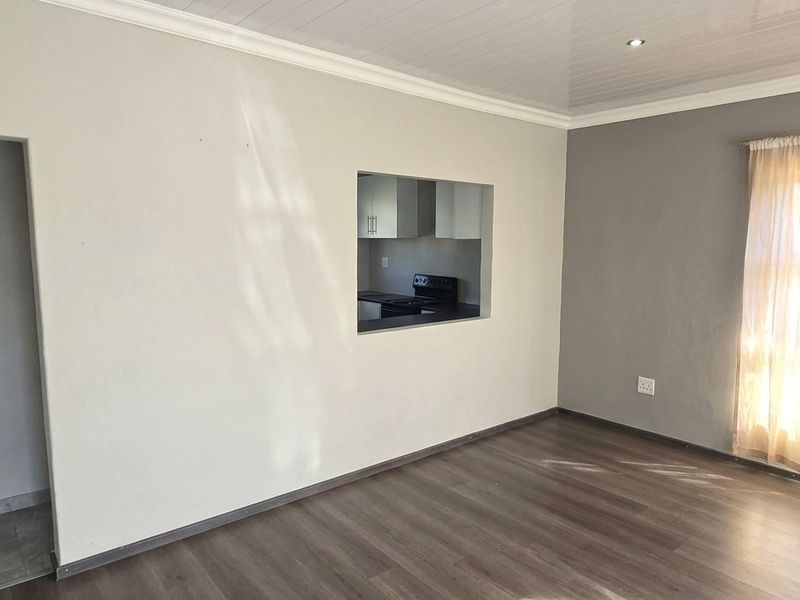 A bright, empty living room featuring modern laminate flooring, neutral walls, and a convenient pass-through window connecting to the kitchen area.