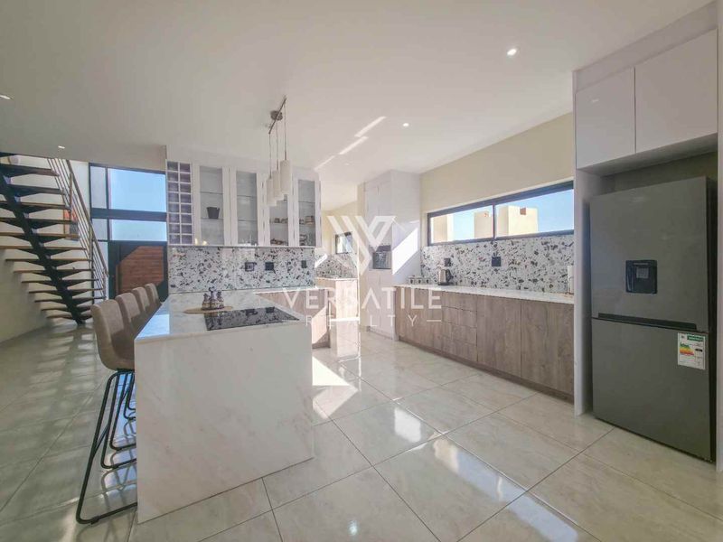 Modern kitchen featuring a central island with stone countertops, sleek cabinetry, and high-quality tiled flooring, seamlessly integrated into an open-plan living space.