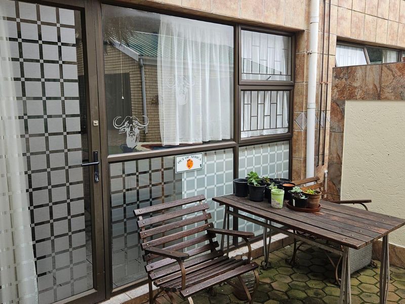 A paved outdoor patio area featuring tiled wall cladding and aluminium-framed glass doors with security bars.