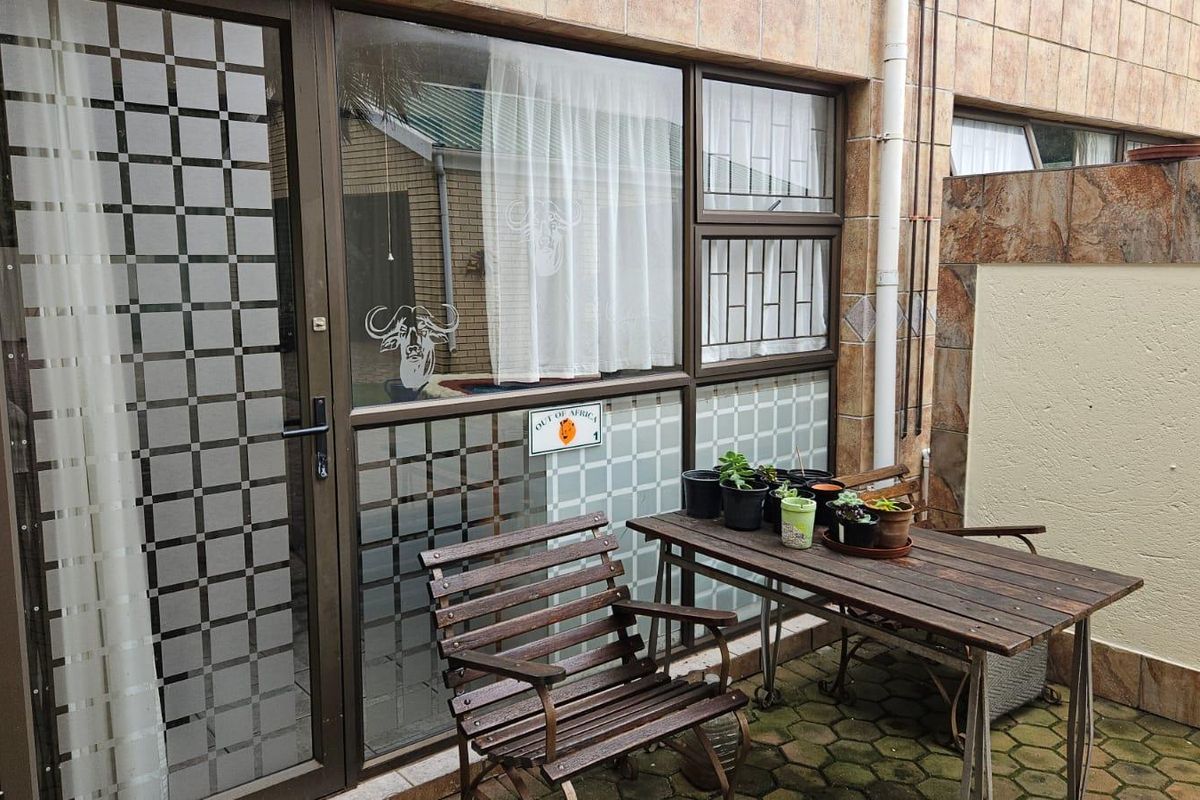 A paved outdoor patio area featuring tiled wall cladding and aluminium-framed glass doors with security bars.