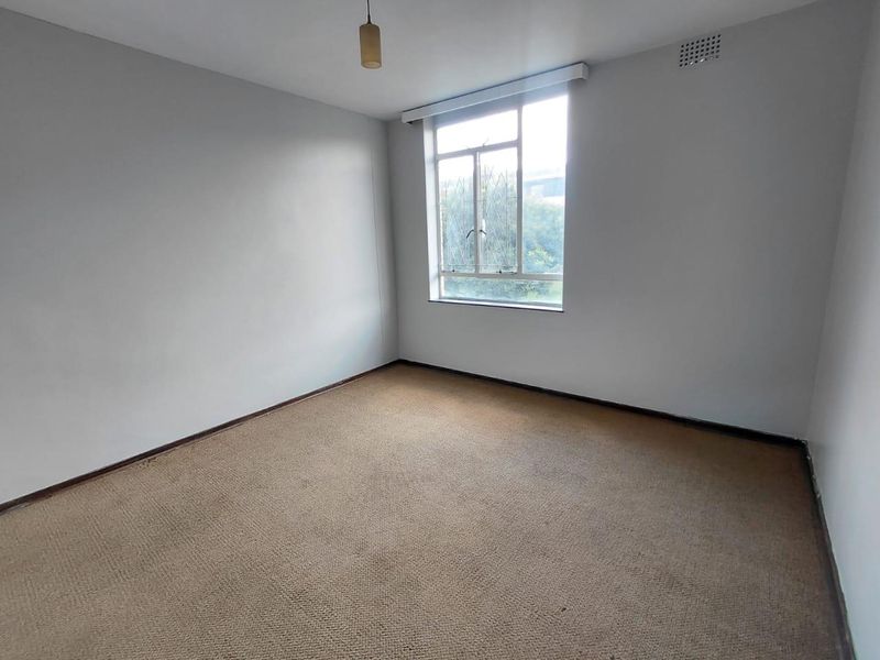 An empty bedroom featuring neutral walls, carpet flooring, and a large window providing natural light.