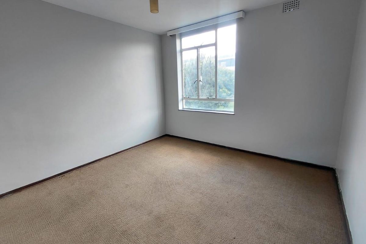 An empty bedroom featuring neutral walls, carpet flooring, and a large window providing natural light.