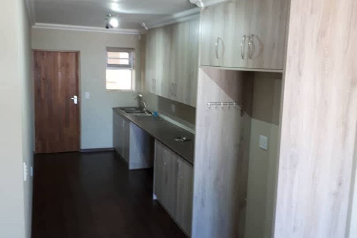 A functional kitchen area featuring light wood-grain cabinetry, dark countertops, and dark laminate flooring, with a dedicated space for a refrigerator.