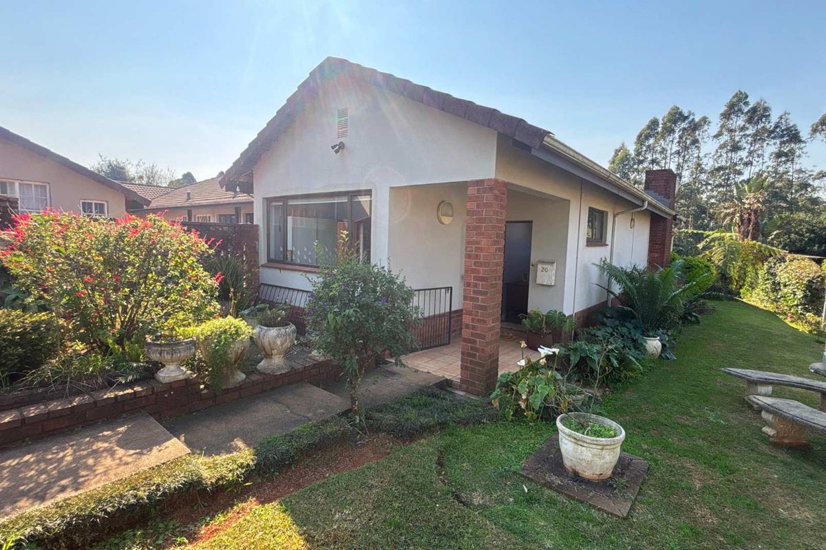 Front elevation of a townhouse featuring a covered entrance, brick pillar detailing, and a well-maintained garden with a concrete pathway.
