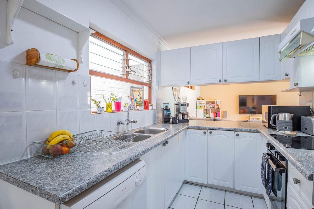 Functional kitchen featuring white cabinetry, granite-look laminate countertops, double stainless steel sink, built-in oven, and hob, with a convenient pass-through window to the living area.