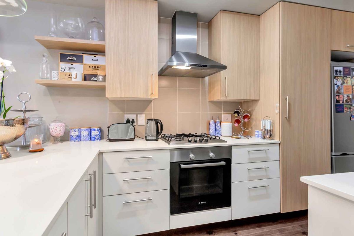 Modern kitchen featuring light wood cabinetry, white stone countertops, a built-in oven, gas hob, and stainless steel extractor fan.