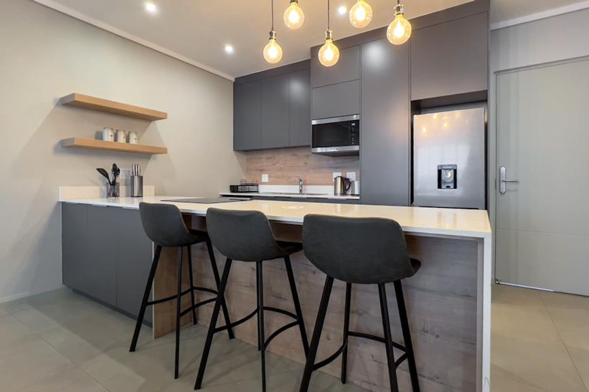 Modern kitchen featuring sleek grey cabinetry, quartz countertops, integrated microwave, floating shelves, and a breakfast bar with stylish pendant lighting.