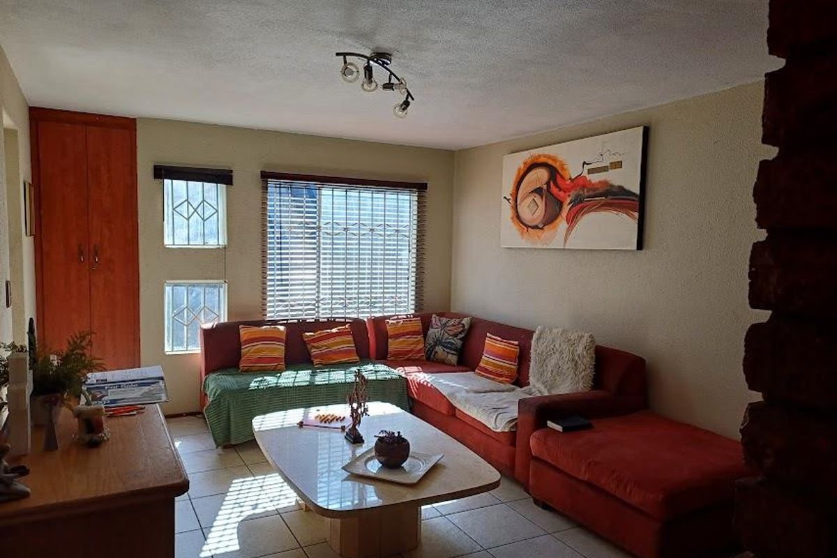 A living room featuring tiled flooring, built-in storage, and natural light through windows fitted with security bars and venetian blinds.