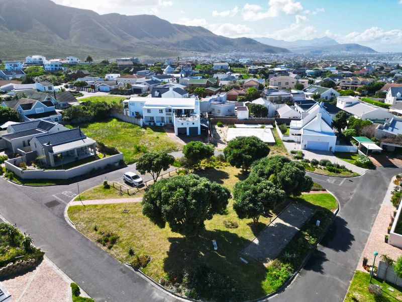 An aerial view of a vacant residential plot situated in a developed coastal neighborhood, featuring established trees and paved street access.