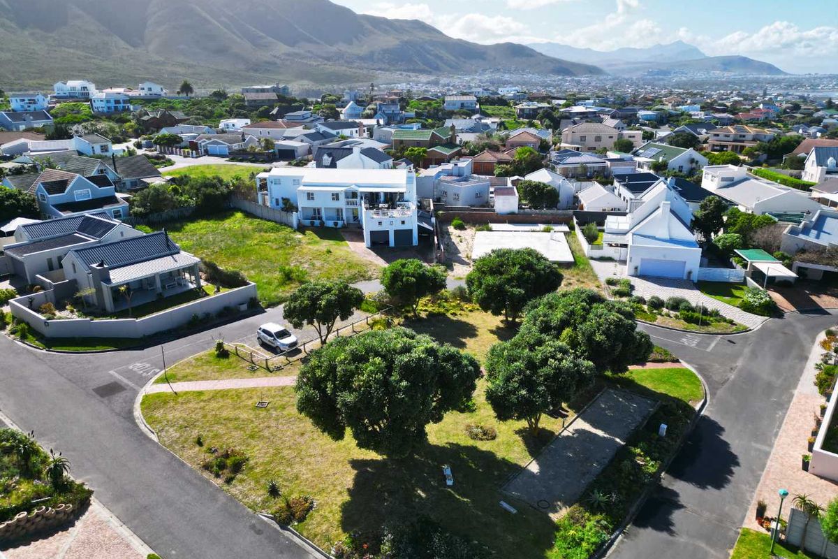 An aerial view of a vacant residential plot situated in a developed coastal neighborhood, featuring established trees and paved street access.