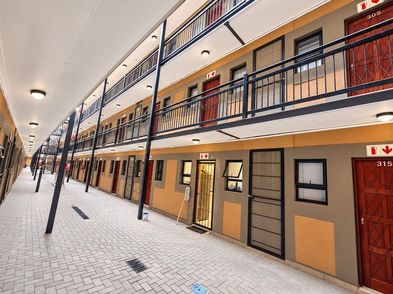 A well-maintained multi-level apartment complex exterior corridor featuring paved walkways, metal security gates, and external lighting.