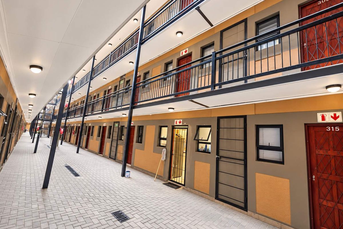 A well-maintained multi-level apartment complex exterior corridor featuring paved walkways, metal security gates, and external lighting.