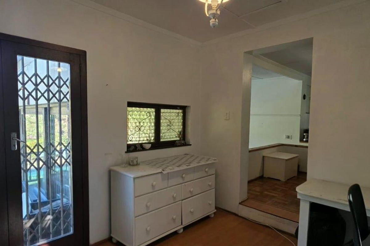 A living area featuring parquet flooring, a security gate leading to the exterior, and built-in shelving, with an adjacent room visible through the doorway.