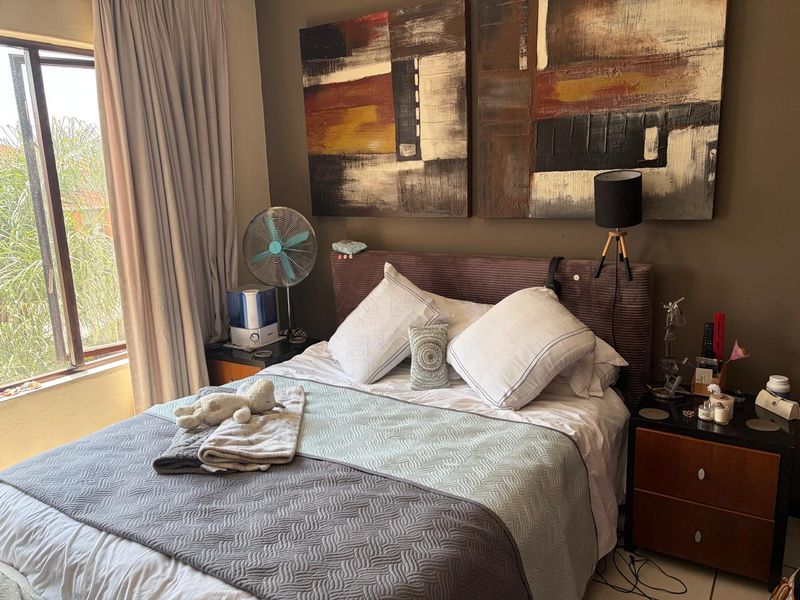 A cozy bedroom featuring a large window with curtains, providing natural light and a view of the exterior greenery.