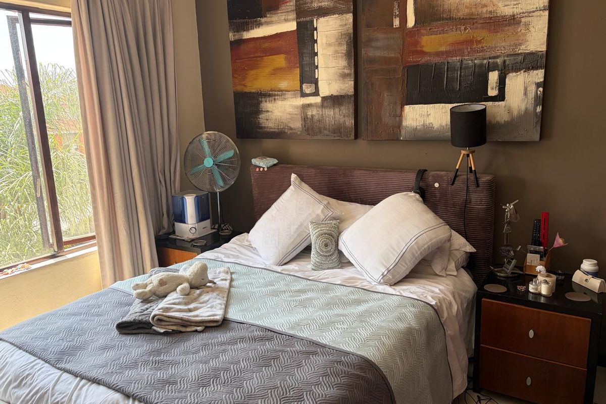 A cozy bedroom featuring a large window with curtains, providing natural light and a view of the exterior greenery.