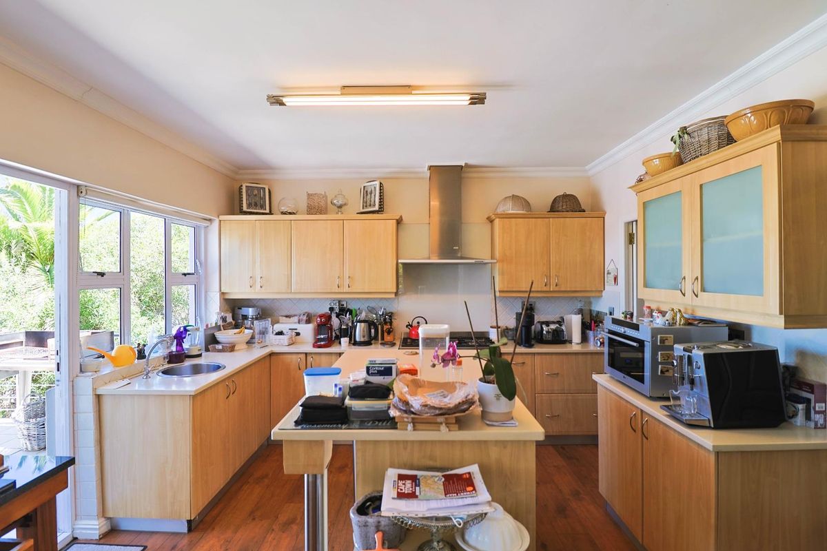 A functional kitchen featuring light wood cabinetry, a central island, stainless steel extractor fan, and direct access to the outdoor area.