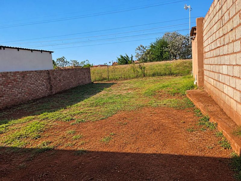 A spacious rear yard area enclosed by brick and concrete block boundary walls, featuring an unlandscaped earth surface.