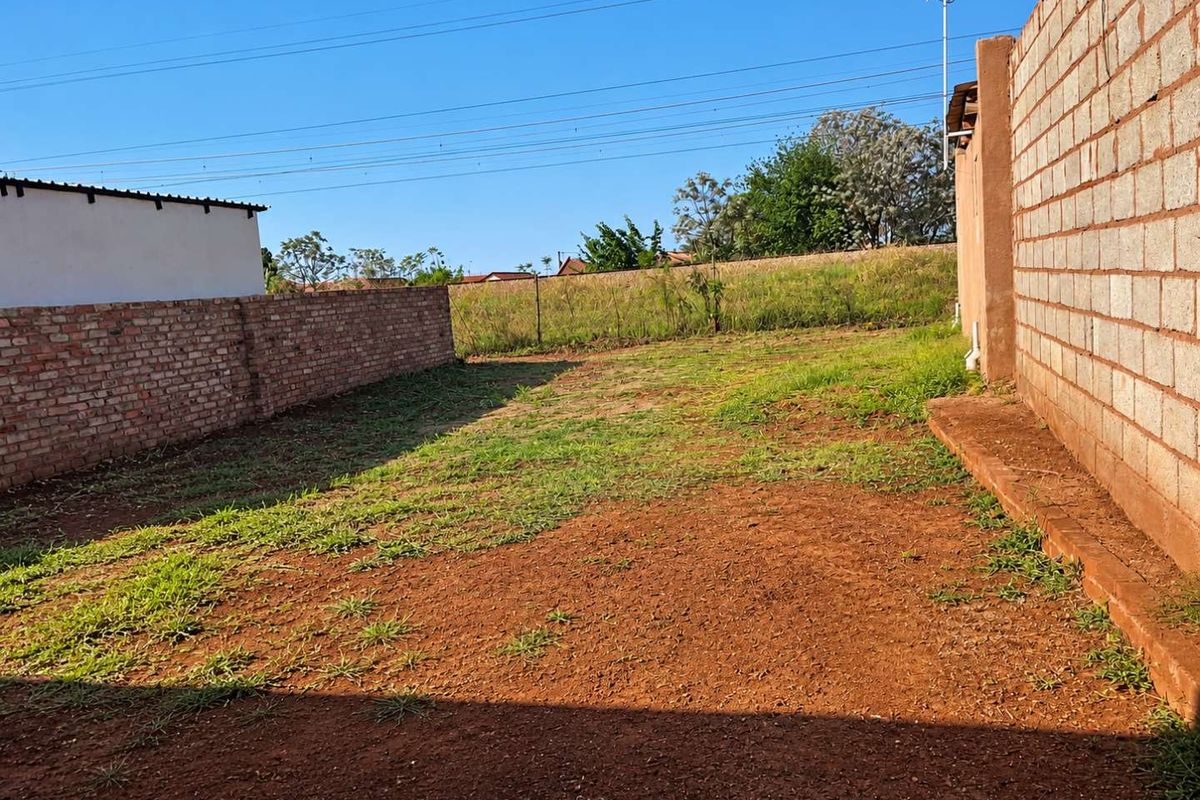 A spacious rear yard area enclosed by brick and concrete block boundary walls, featuring an unlandscaped earth surface.