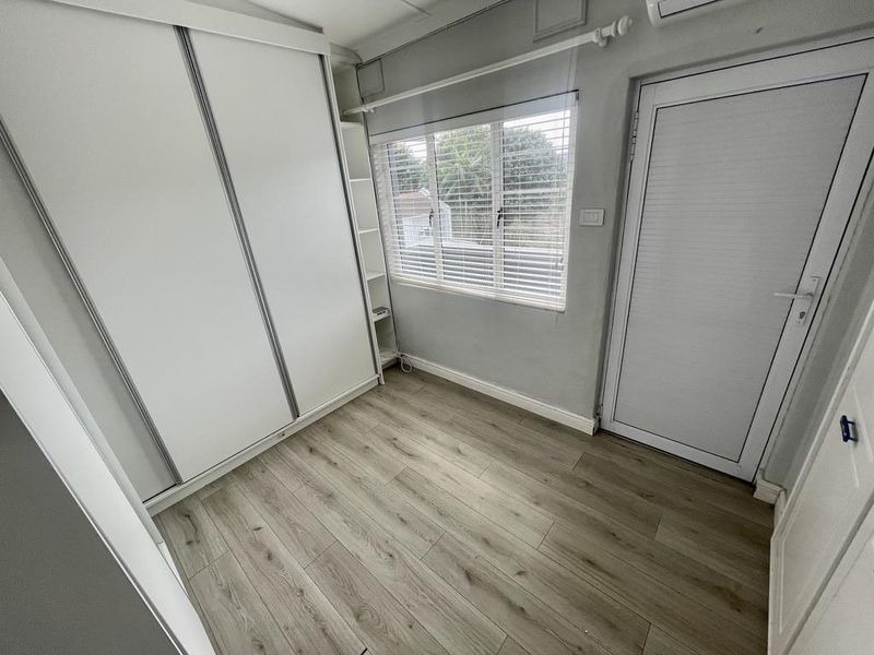 A clean, empty bedroom featuring light wood-look laminate flooring, a large built-in wardrobe, window blinds, and a wall-mounted air conditioning unit.
