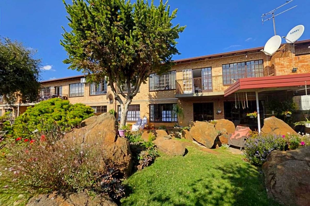 Rear view of a multi-story townhouse featuring a landscaped garden with large rock features, a lawn, and a balcony overlooking the outdoor space.