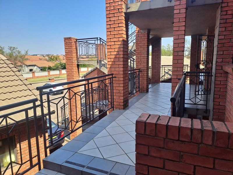 An elevated balcony area featuring exposed brick pillars, metal safety railings, and tiled flooring, providing access to the apartment exterior.