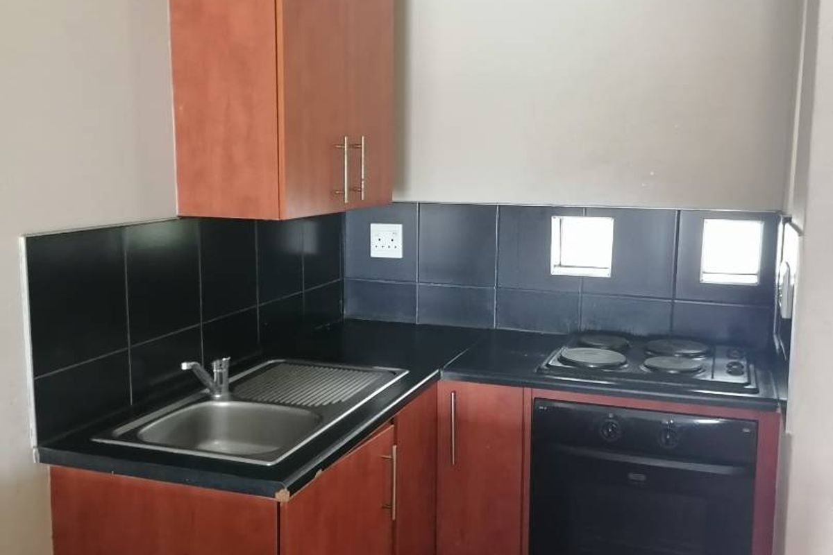 Compact kitchen featuring laminate cabinetry, a stainless steel sink, built-in oven, electric hob, and a black tiled splashback.