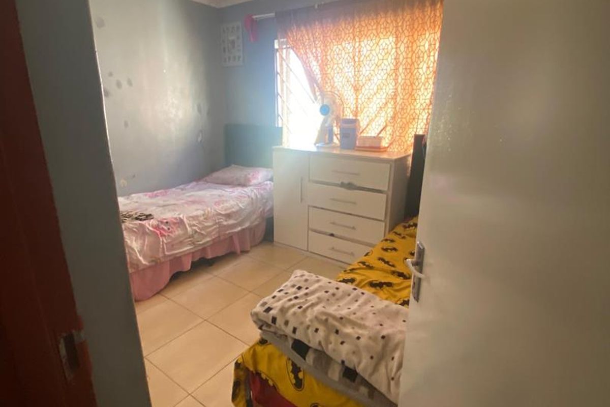 A bedroom featuring tiled flooring and a window with a security gate. The walls show signs of wear and require maintenance.