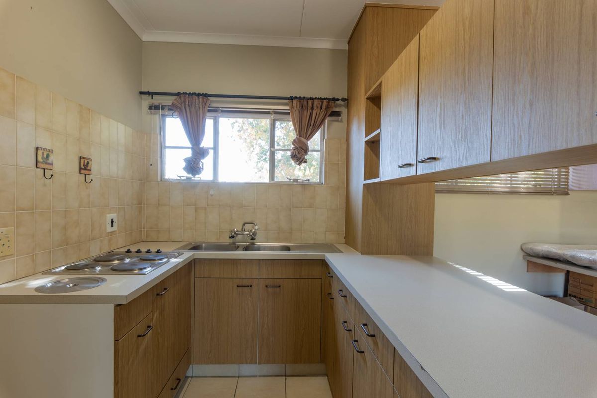 A functional kitchen featuring wood-look laminate cabinetry, ample countertop space, a double basin sink, and an integrated electric hob with tiled backsplash.