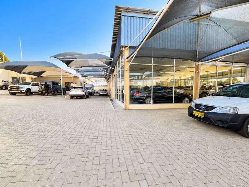 A commercial retail property featuring a paved forecourt with extensive shade cloth parking structures and large glass display windows for vehicle showroom use.