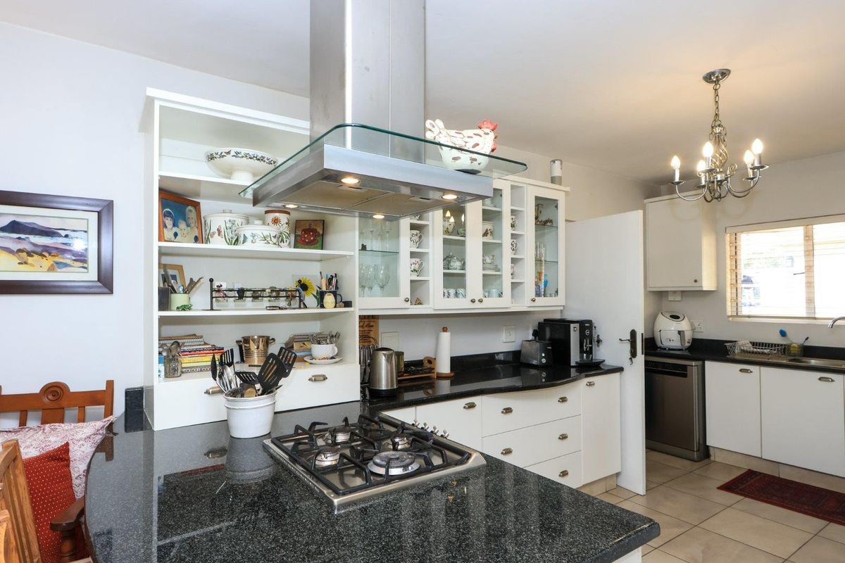 A functional kitchen featuring granite countertops, a gas hob with overhead extractor, ample cabinetry, and tiled flooring, offering a practical layout for daily cooking.