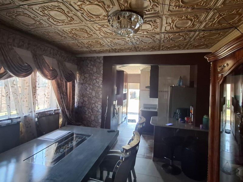 Open plan living and dining area featuring decorative ceiling tiles, stone accent wall, and a breakfast bar connecting to the kitchen space.