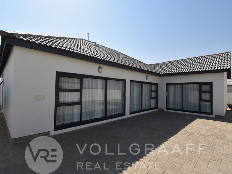 Rear exterior view of the property featuring a paved patio area and large sliding glass doors leading into the home.