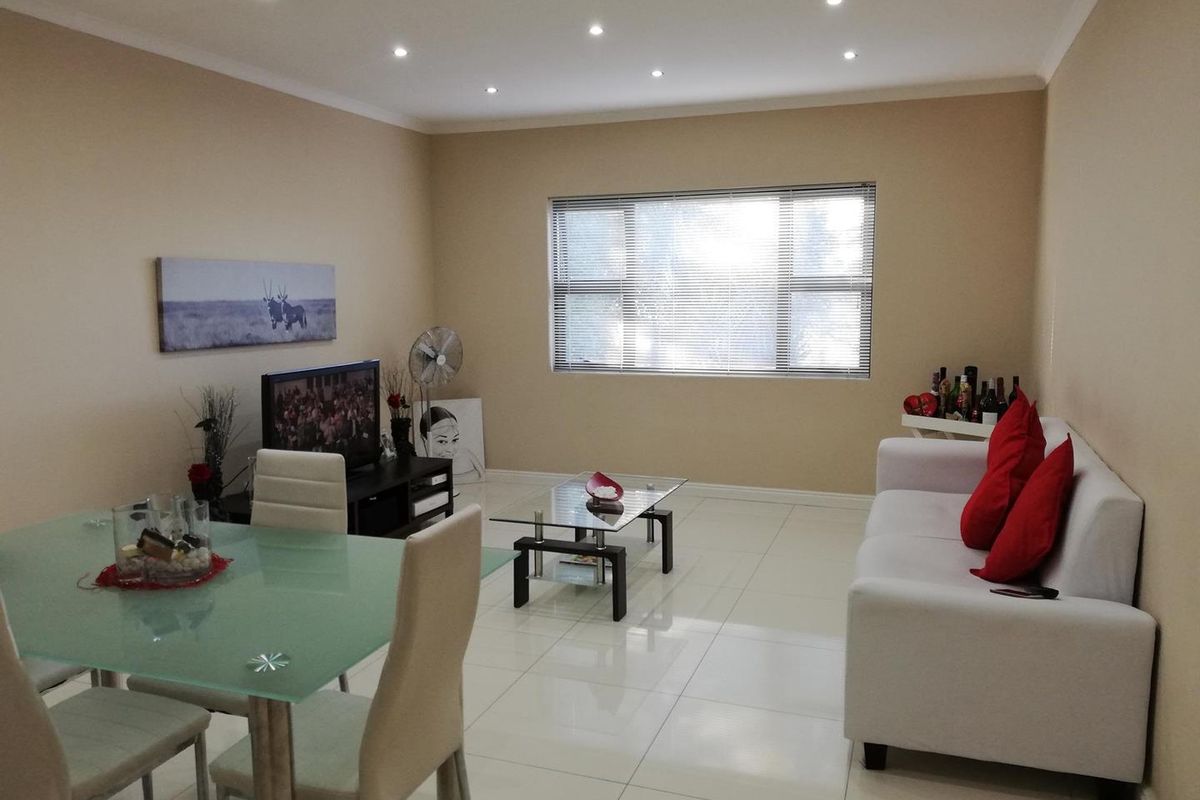 Open plan living and dining area featuring neutral tiled flooring, recessed downlighting, and large windows with fitted venetian blinds.