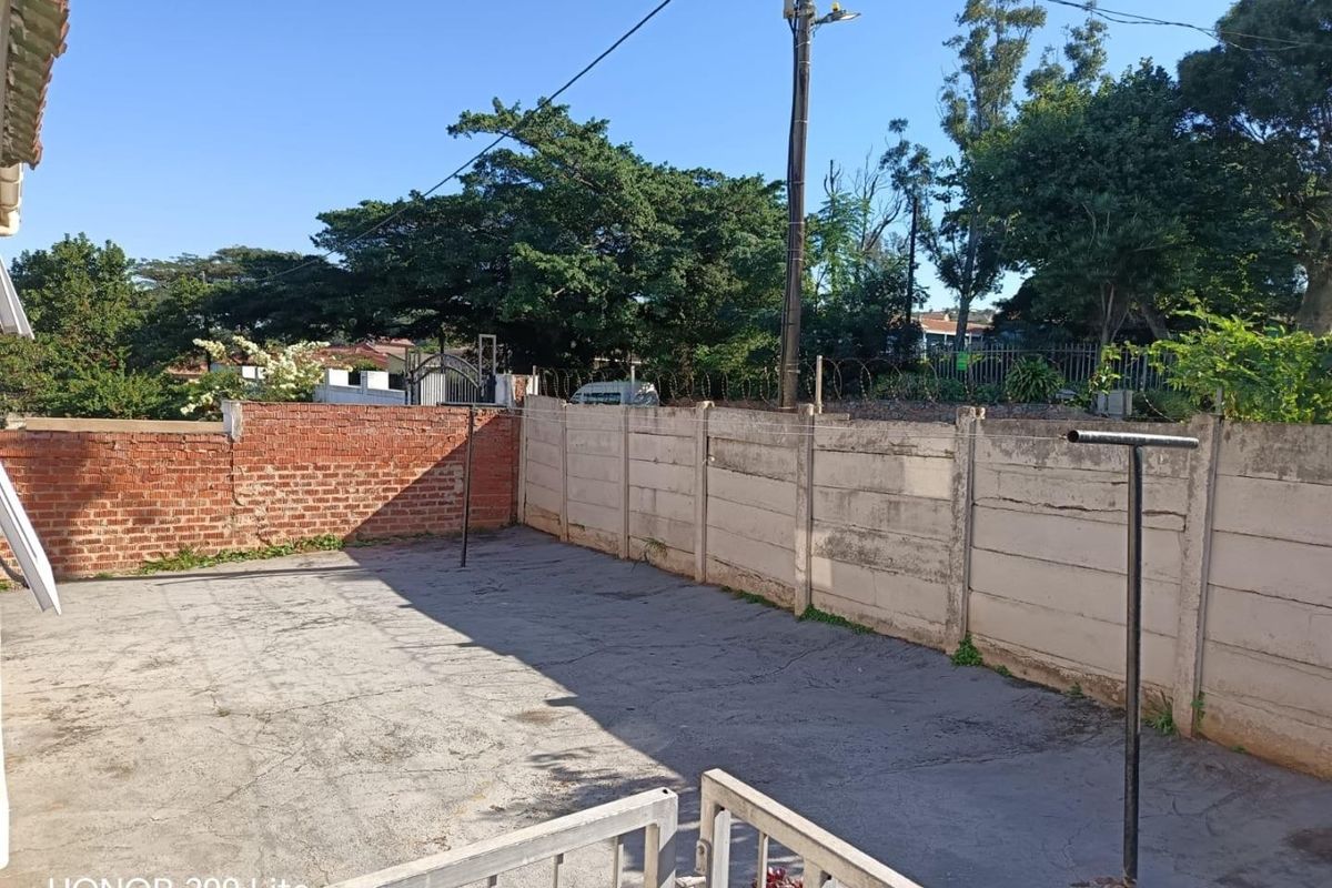 A rear courtyard area featuring concrete paving, brick and precast concrete boundary walls, and a fixed metal washing line.