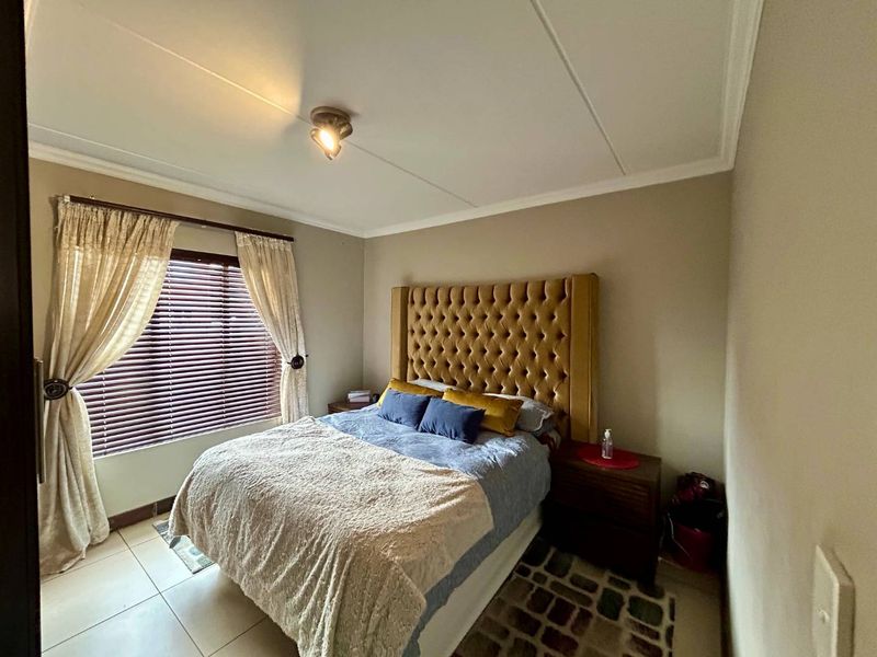 A bedroom featuring tiled flooring, neutral wall tones, and window treatments including venetian blinds and curtains.