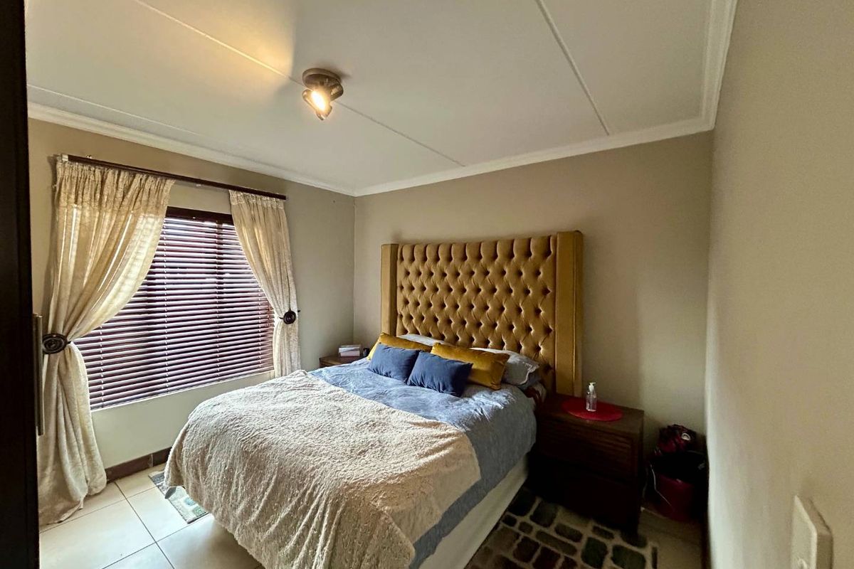 A bedroom featuring tiled flooring, neutral wall tones, and window treatments including venetian blinds and curtains.